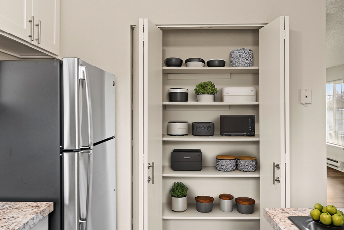 Stylish kitchen with well-organized shelves featuring modern containers, plants, and a sleek stainless steel fridge.
