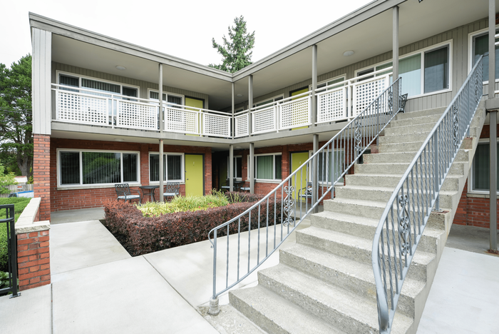 Inviting two-story apartment building with exterior stairway and patio seating area.