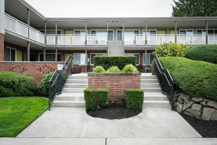Inviting exterior of a two-story apartment building with a landscaped entrance and balcony access.