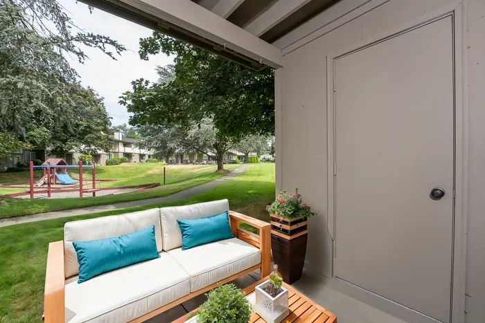 Cozy patio setup with a comfy couch, overlooking a garden with a playground and lush greenery.