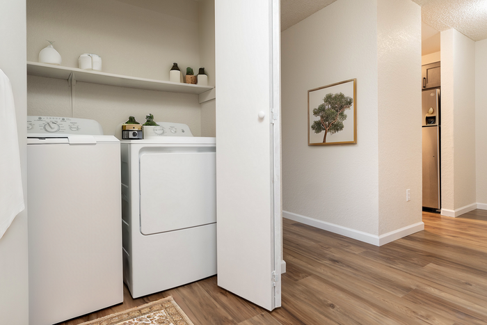 Modern laundry area with washer and dryer on sleek hardwood flooring, featuring minimalist shelving and elegant decor.