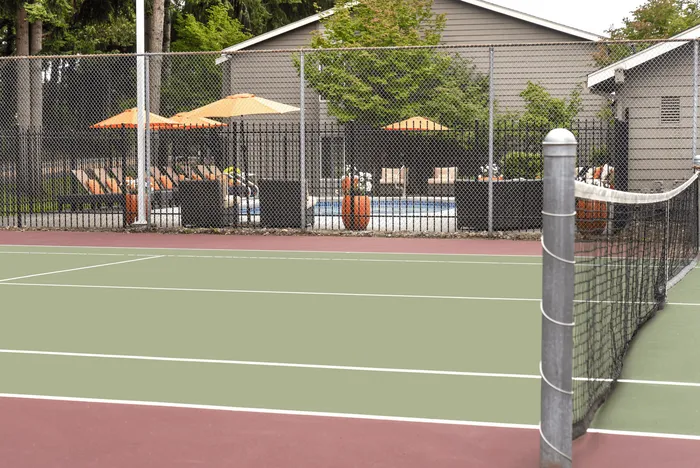 Inviting outdoor pool area with loungers and umbrellas adjacent to a tennis court at a modern apartment complex.
