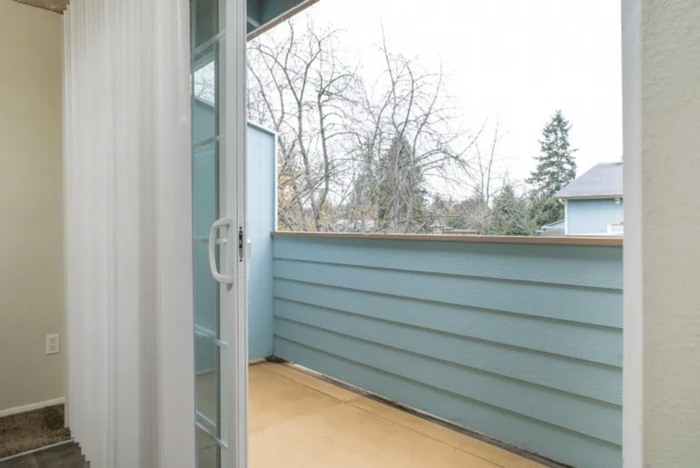Inviting balcony area with glass sliding doors and a view of lush trees and rooftops.