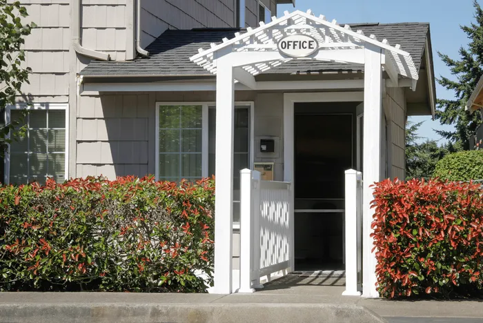 Inviting exterior entrance to a residential office, framed by lush greenery and a welcoming white pergola.