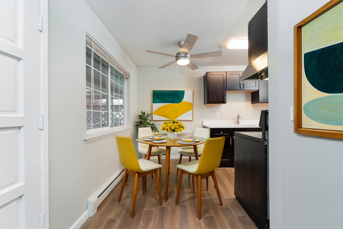 Contemporary dining space with a round table set for four, adjacent to a modern kitchen with stylish dark cabinets.