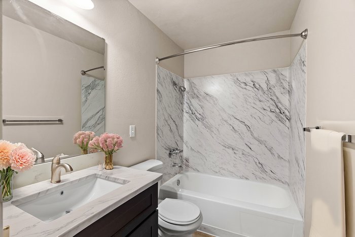Bright modern bathroom with marble shower, elegant sink, and fresh floral decor.