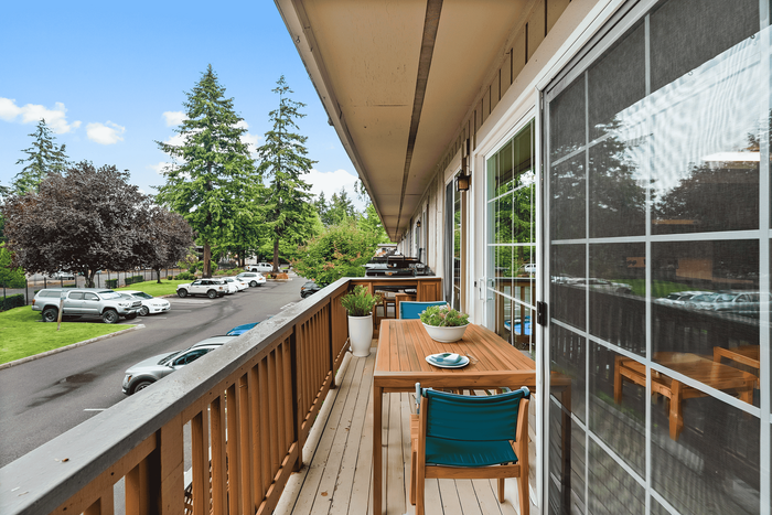 Charming balcony view with wooden furniture overlooking a lush green area and parked cars.