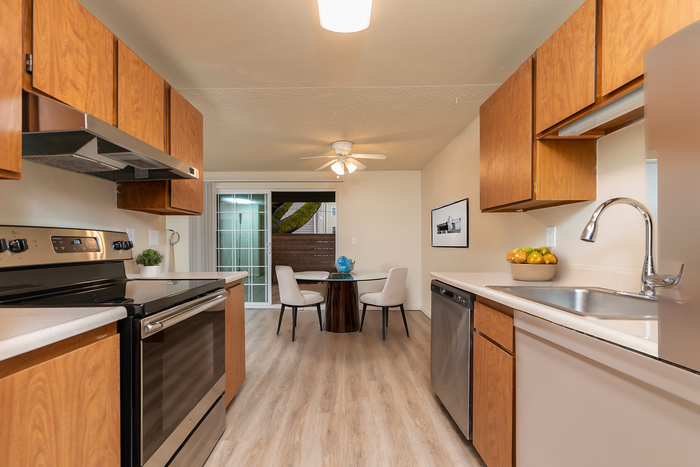 Inviting kitchen with wooden cabinetry, stainless steel appliances, and an adjacent dining area featuring a modern table with chairs, illuminated by natural light through sliding glass doors.