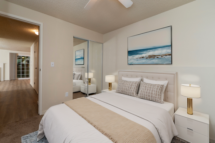 Inviting bedroom featuring a comfortable bed, stylish decor, and a mirrored closet with a view into an elegant hallway.