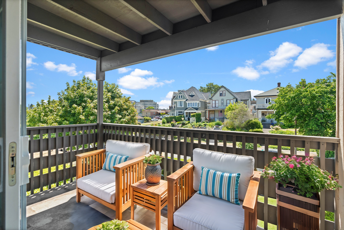 Inviting balcony with cozy seating and a picturesque view of lush neighborhood gardens.