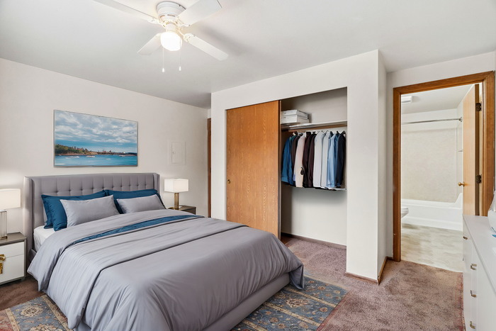 Comfortable bedroom with gray bedding, open closet, and modern decor featuring a landscape painting.