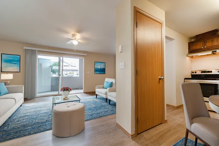 Bright and airy living room with plush seating, large windows, and a glimpse of the kitchen area.