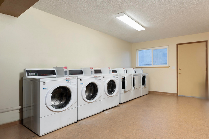 Modern laundry room with a row of six energy-efficient washing machines under bright lighting.