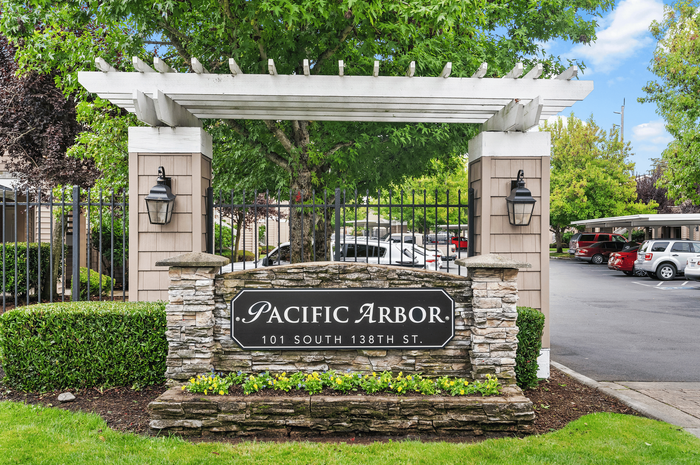 Charming entrance of Pacific Arbor featuring lush greenery, elegant stone sign, and classic lanterns.