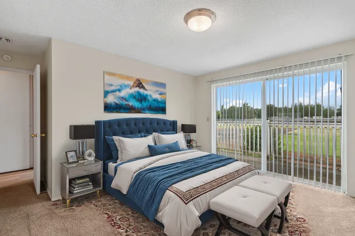 Inviting bedroom with plush blue bed, elegant decor, and large window offering scenic views of lush greenery.