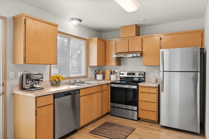 Modern kitchen with natural wood cabinets, stainless steel appliances, and ample counter space, bathed in natural light from a large window.