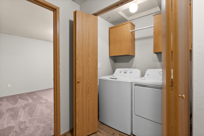 Convenient in-unit laundry area featuring modern washer and dryer, complemented by spacious storage cabinets and natural wood accents.