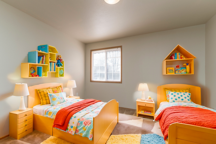 Charming children's bedroom with twin beds, vibrant bedding, and playful shelving, creating a cozy and inviting atmosphere.