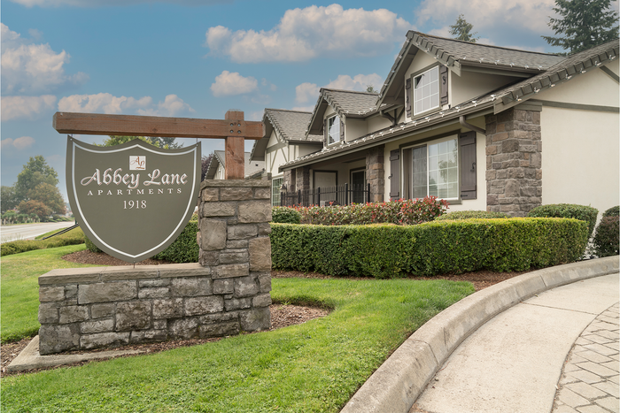 Charming entrance to Abbey Lane Apartments surrounded by manicured gardens and elegant stone features, under a picturesque sky.