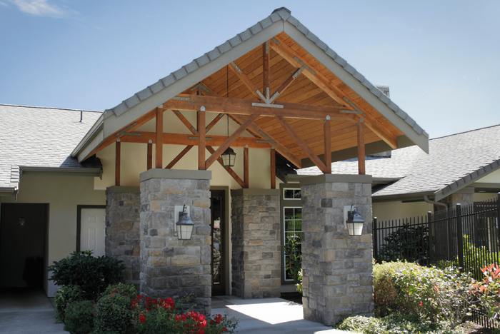 Inviting entrance with charming stone columns, elegant wooden beams, and lush greenery, showcasing modern architectural design.