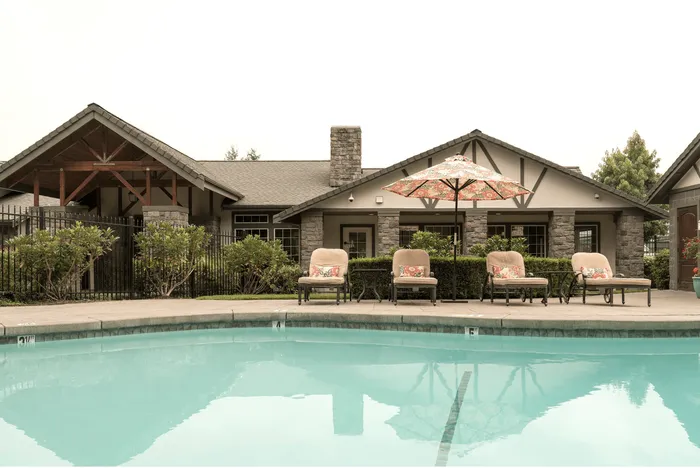 Elegant apartment complex with cozy outdoor seating by a refreshing pool, surrounded by lush greenery and rustic architecture.