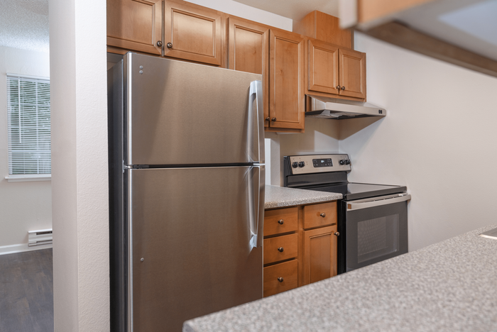 A modern kitchen featuring stainless steel appliances, wood cabinetry, and a speckled countertop with a built-in sink.