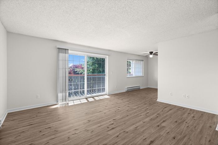 Bright and airy living room with stylish wood flooring, large windows, and a sliding glass door to a sunlit balcony.