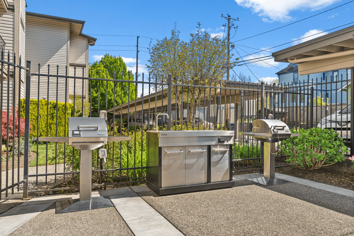 Bright outdoor patio with a round table, chairs, and an ornamental umbrella beside stainless steel grills.