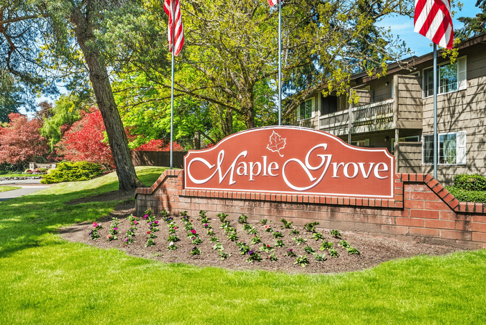 Charming apartment building set amidst lush greenery, with flags and a welcoming sign for Maple Grove.