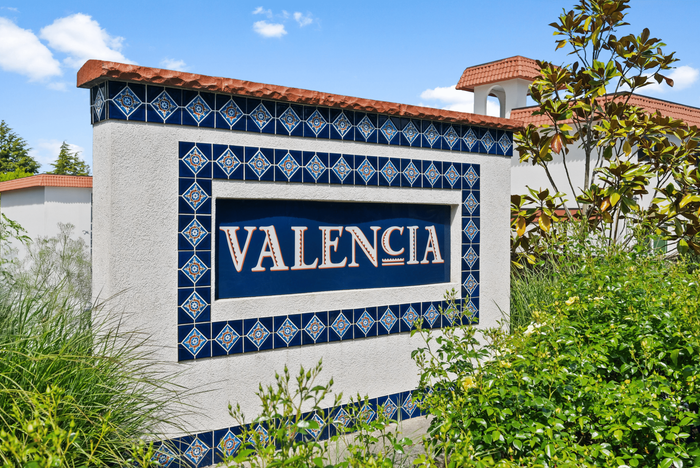 Elegant entrance sign for Valencia Apartments, featuring stylish blue and white tile design amid lush greenery, offering a warm welcome.