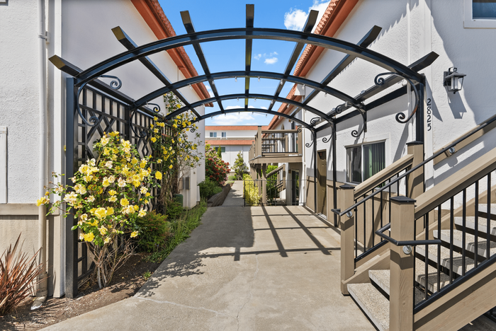 Charming apartment entrance with elegant pergola and blooming yellow flowers, creating a welcoming atmosphere.
