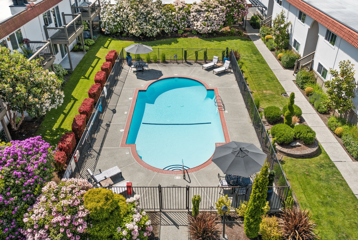 Charming apartment complex showcasing a beautifully landscaped courtyard with a refreshing pool, vibrant flower gardens, and inviting lounge chairs.