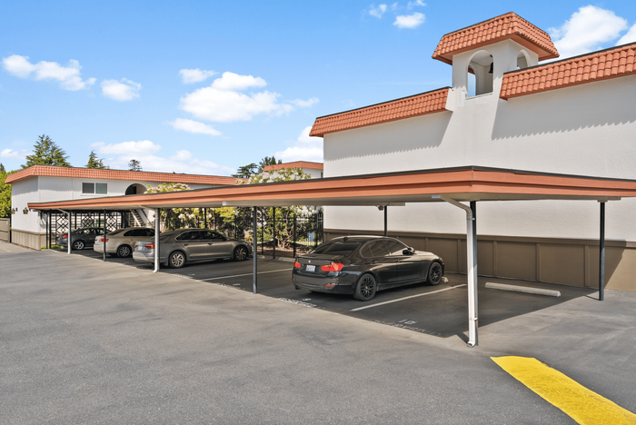 Modern apartment complex with ample covered parking, featuring sleek architecture and vibrant terra-cotta roofs under a clear blue sky.