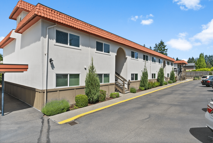 Charming apartment building with a Mediterranean-style terracotta roof, surrounded by well-maintained greenery and ample parking space.