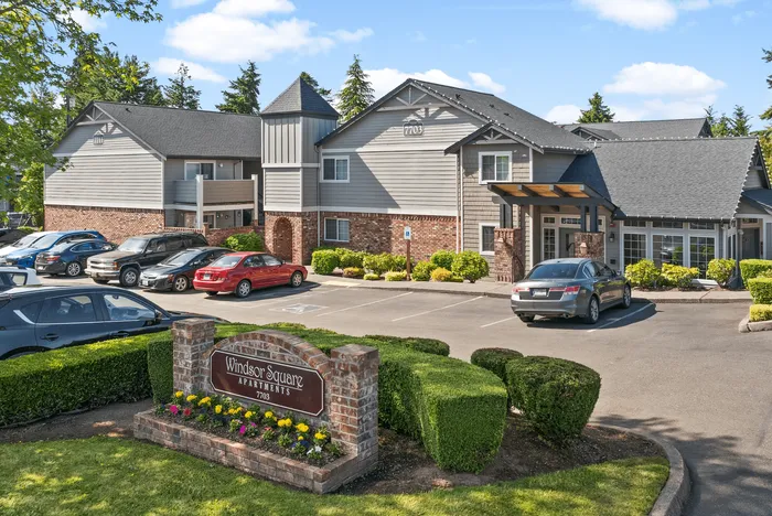 Charming Windsor Square Apartments showcasing beautiful landscaping, ample parking, and inviting architectural design under a clear blue sky.