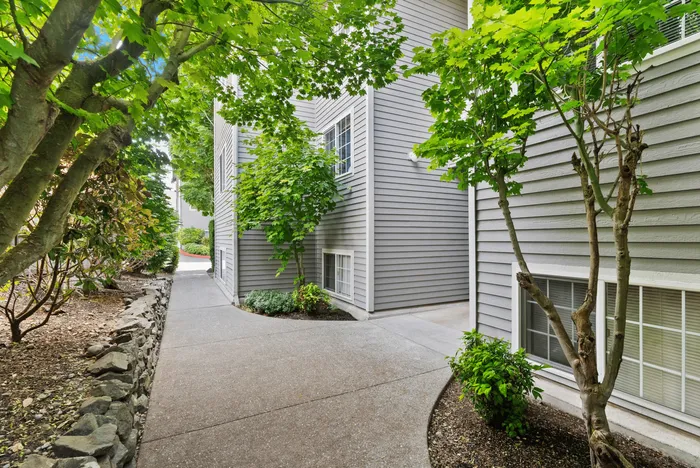 Charming apartment exterior with modern gray siding, lush greenery, and serene garden walkway.