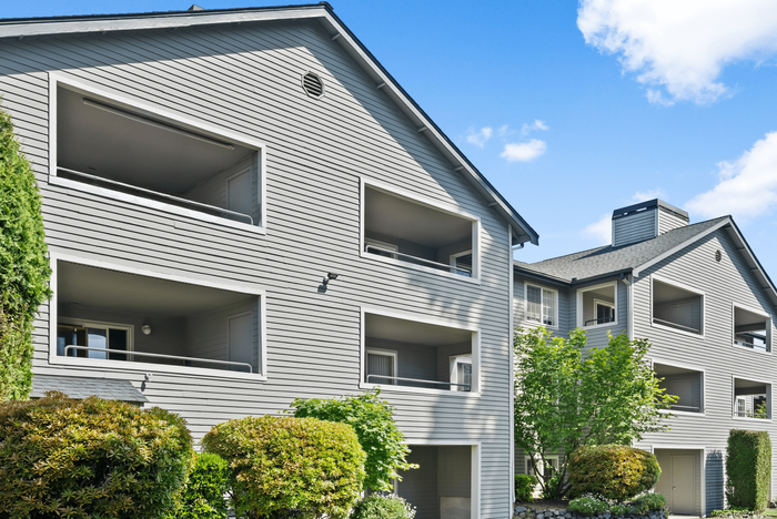 Multi-story apartment building with spacious balconies, surrounded by lush greenery, under a vibrant blue sky.