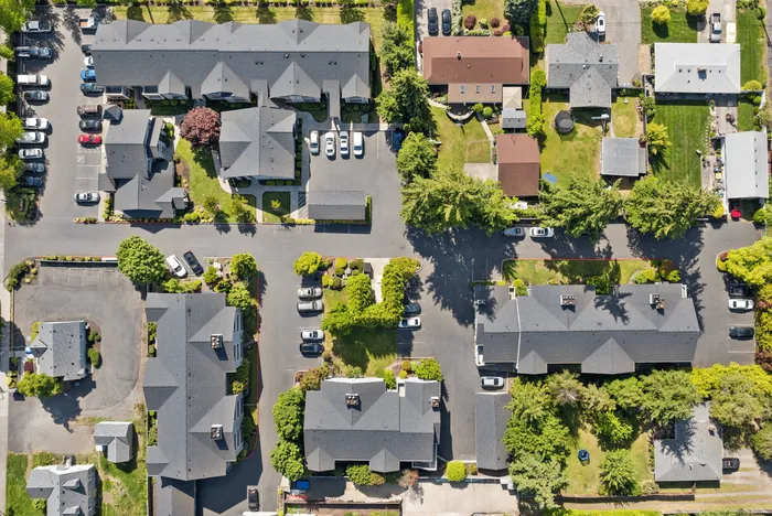Captivating aerial view of a modern apartment complex surrounded by lush greenery and ample parking, showcasing a harmonious blend of nature and urban living.