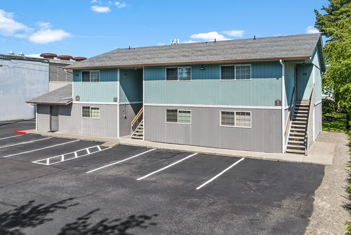 Charming two-story apartment building with fresh exterior, ample parking, and inviting natural surroundings.