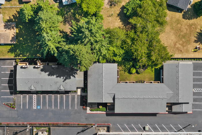 Aerial view of modern apartment complex surrounded by lush greenery, featuring ample parking and a private natural setting.