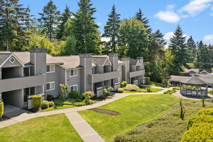 Apartment complex surrounded by lush greenery and manicured lawns, featuring modern architectural design and a picturesque gazebo.