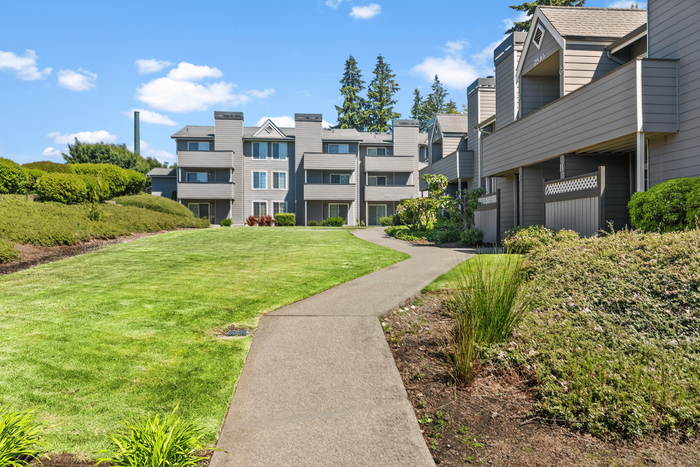 Apartment complex set amidst lush greenery with a beautifully manicured lawn and clear blue skies.