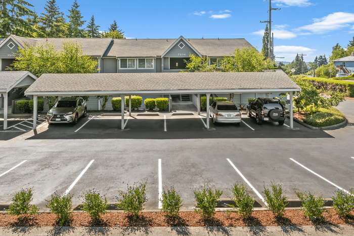 Inviting apartment complex exterior with a well-maintained covered parking area, surrounded by lush greenery and vibrant landscaping.