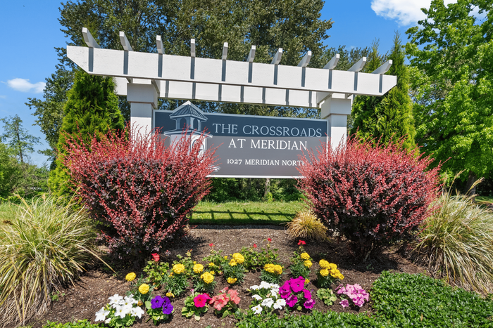 Welcoming entrance sign for The Crossroads at Meridian, beautifully landscaped with vibrant flowers and lush greenery.