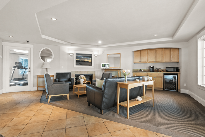Elegant communal living area featuring plush leather seating, a cozy fireplace, and a kitchen nook with modern cabinetry in a stylish apartment complex.