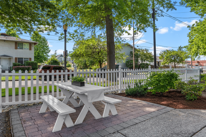 Outdoor space with a white picket fence, featuring a cozy picnic table on a well-maintained patio surrounded by lush greenery.