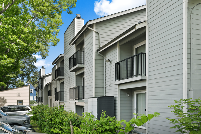 Elegant apartment building with modern balconies and lush greenery, set against a bright blue sky.