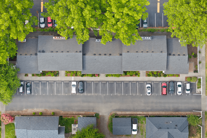Aerial view of modern apartment buildings surrounded by lush greenery, featuring ample parking space and a well-maintained neighborhood.