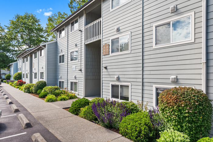 Charming gray apartment building with lush landscaping and sunny views, ideal for modern living.