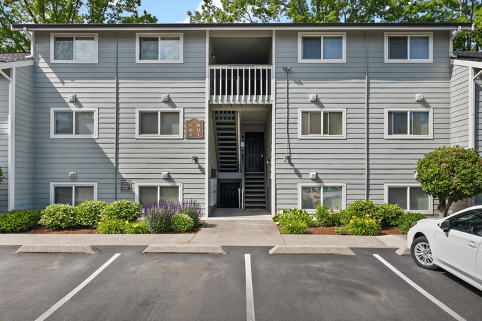 Modern apartment building exterior with grey siding, lush landscaping, and convenient parking space.